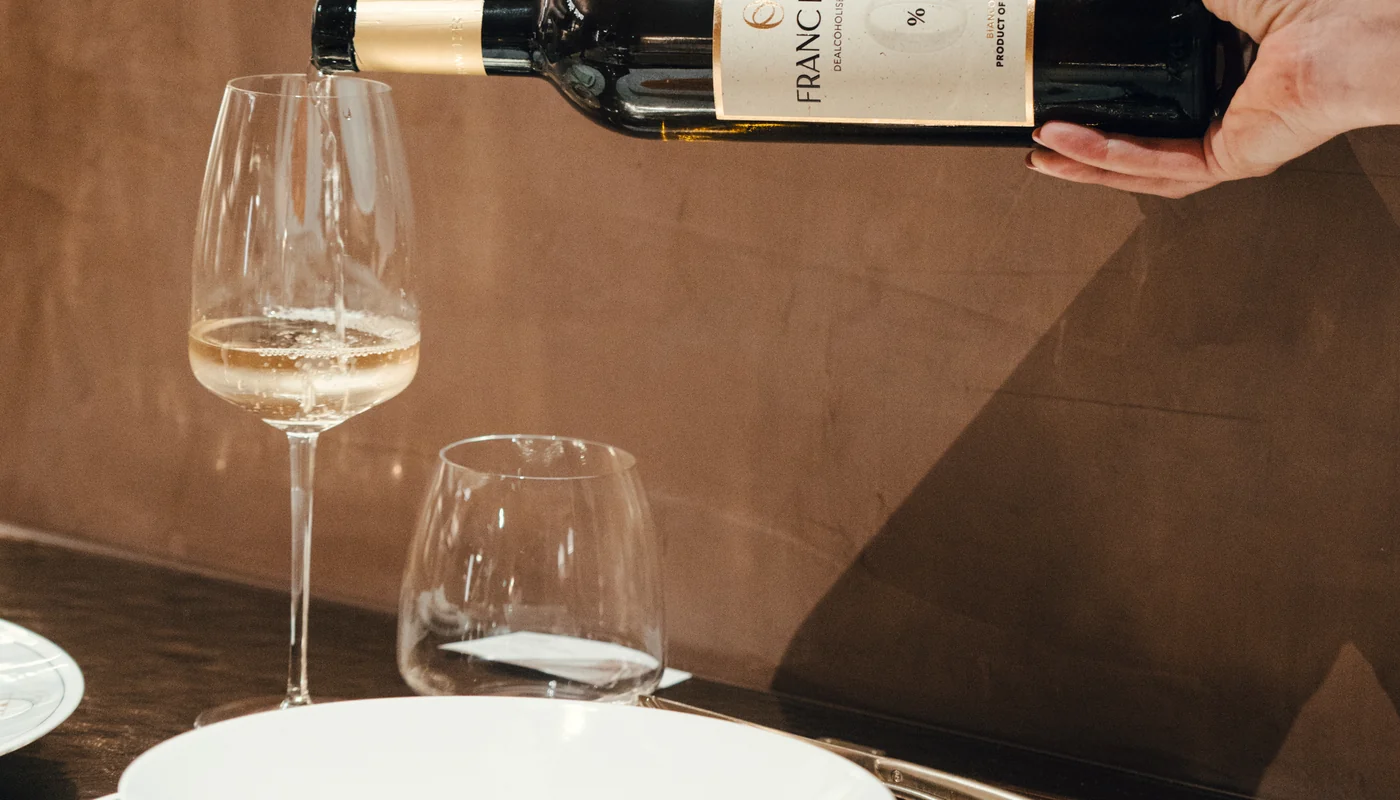 Vin alb turnat într-un pahar, pe o masă pregătită pentru cină